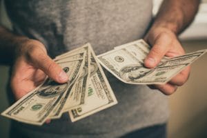 A man in a gray t-shirt holds eight hundred-dollar bills in his hands.